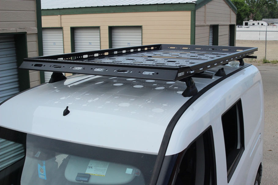 A Large Black Revrack tray atop a newer style White Van, parked near enclosed storage units