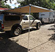 8 foot wide weather awning attached to a medium Revrack Tray, atop a two thousand four gold toyota tacoma pickup truck with gold topper shell