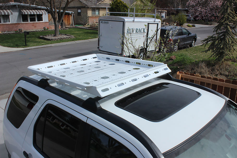 Small white revrack tray atop a white two thousand four honda crv with en enclosed white trailer in the neighborhood background