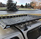 a medium sized black revrack tray atop a gold toyota tacoma with gold topper shell, with a pond and trees in the background