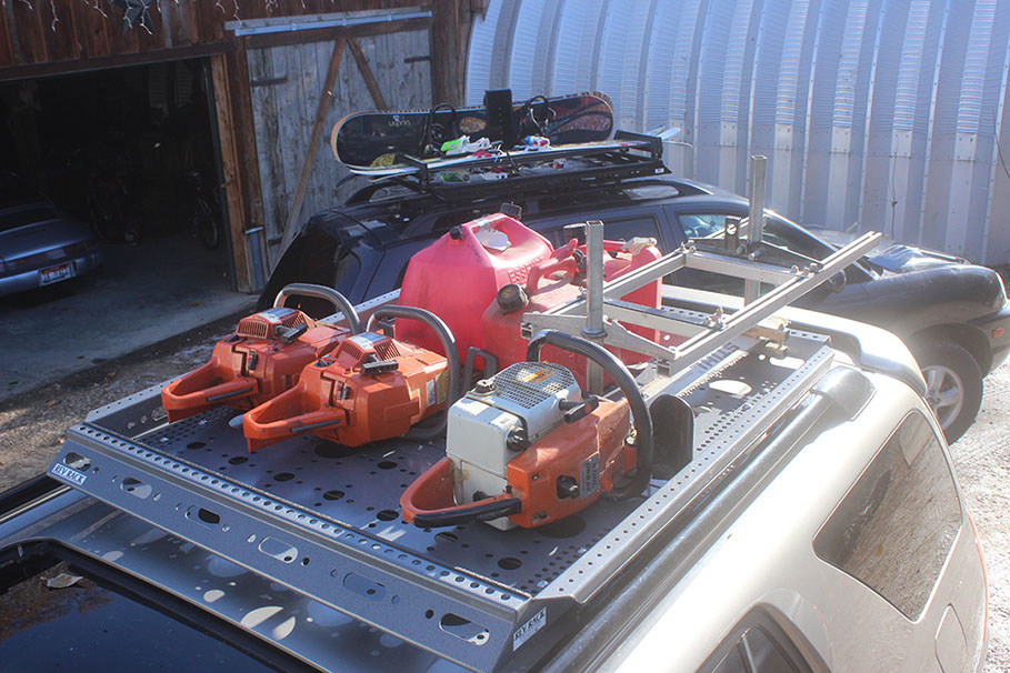 three orange and white chainsaws and red fuel cans in a revrack tray atop a gold nissan pathfinder