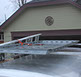 looking down at a large grey colored revrack atop a white enclosed trailer with a light brown house with burgundy trim in the background