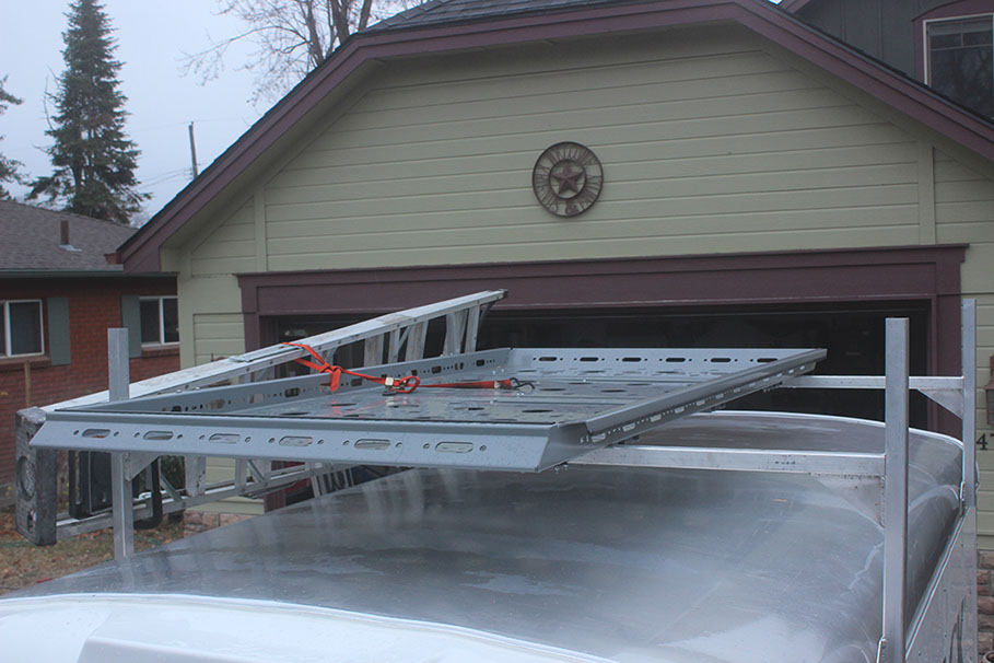 looking down at a large grey colored revrack atop a white enclosed trailer with a light brown house with burgundy trim in the background