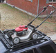 looking down at a red and silver lawnmower sitting in a small black revrack tray atop a navy blue hun die in a neighborhood driveway