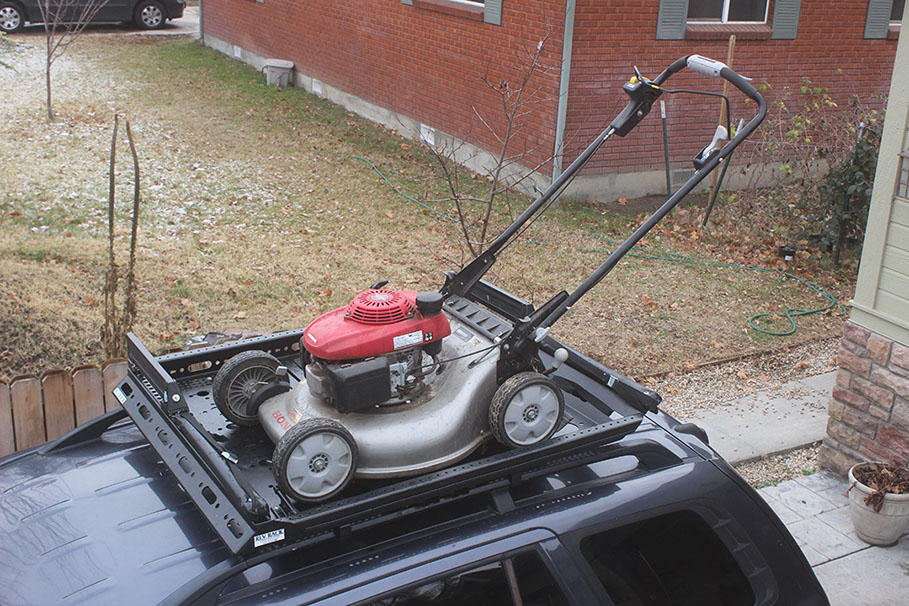 looking down at a red and silver lawnmower sitting in a small black revrack tray atop a navy blue hun die in a neighborhood driveway