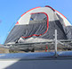 looking up at a dome shaped tan and grey tent with red trim sitting n a large silver revrack atop a white enclosed trailer
