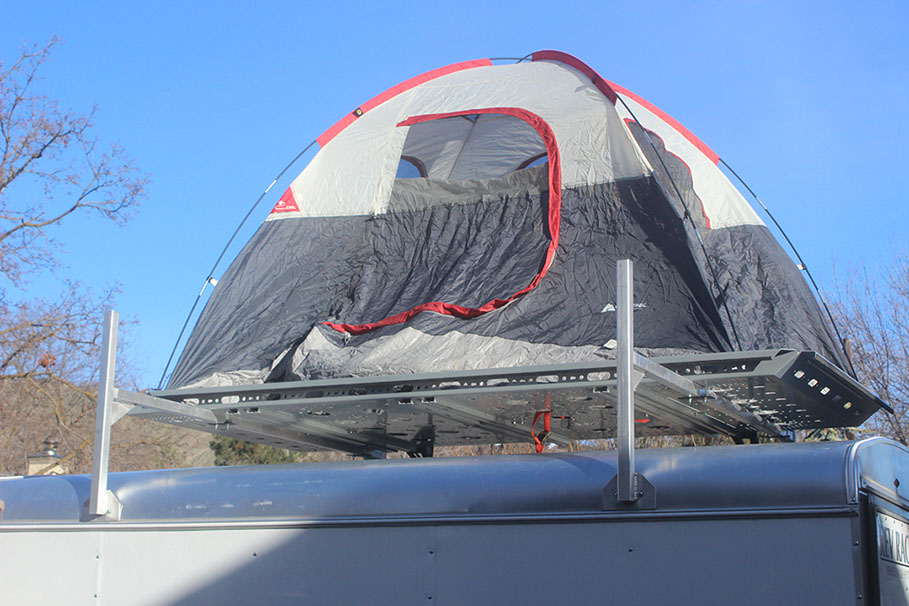 looking up at a dome shaped tan and grey tent with red trim sitting n a large silver revrack atop a white enclosed trailer